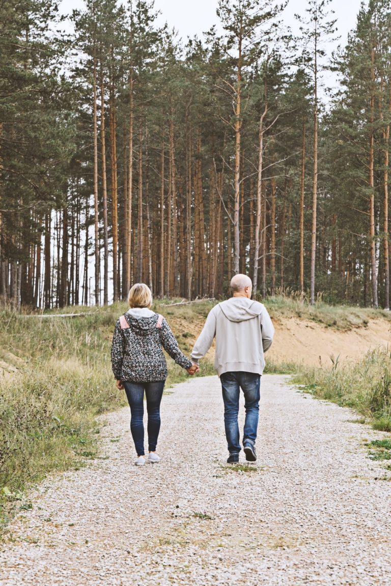 Middle-aged couple of baby boomers people behind walking in forest and enjoying sunny autumn evening